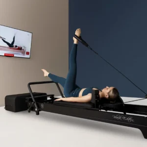 kobieta ćwiczy na łożku reformer. pozycja leżąca pilates wzmacniającą tylną taśmę, na telewizorze wyświetla się obraz pokazujący jak wykonywać ćwiczenie pilates